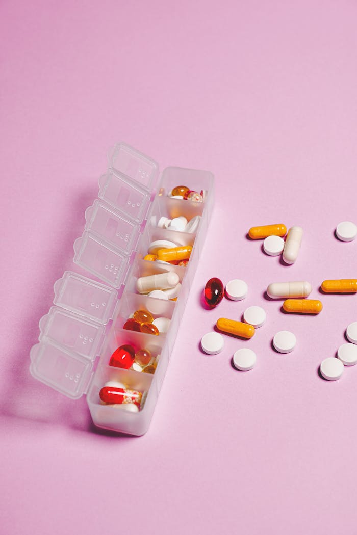 services-02 Colorful assortment of pills and capsules in organizer on pink backdrop.