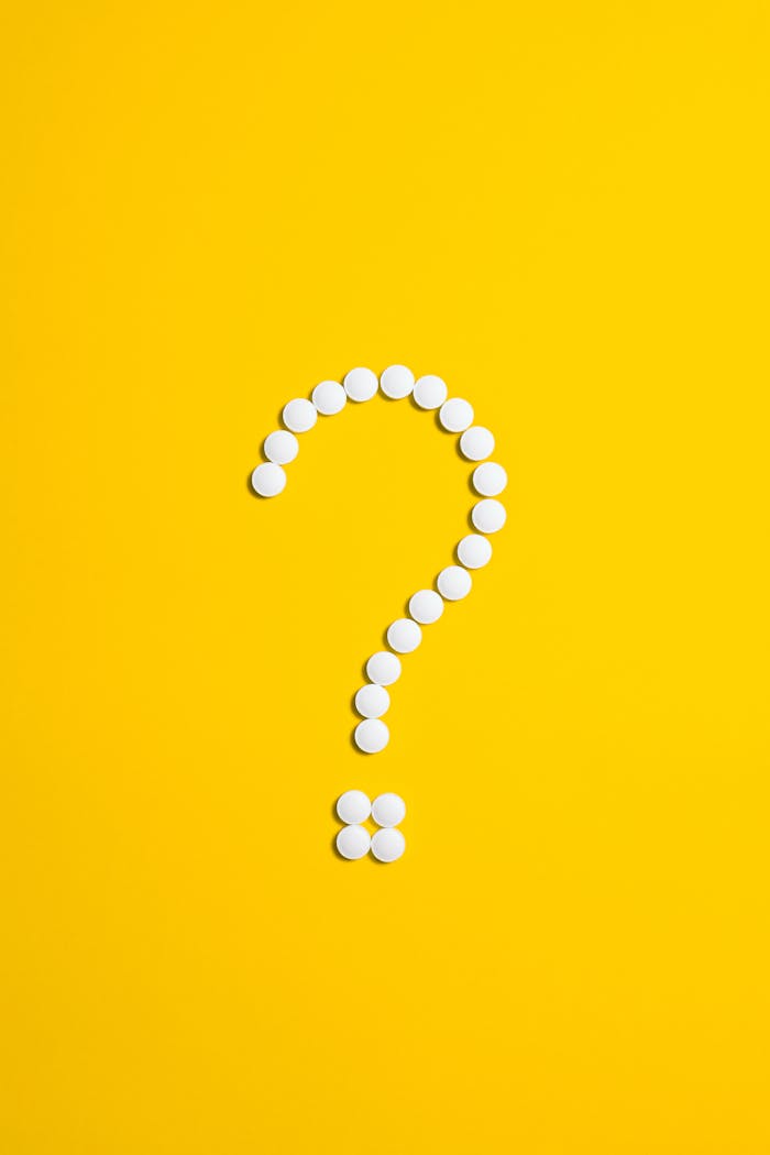 services-01 White pills arranged in a question mark shape on a bright yellow background, symbolizing medical queries.